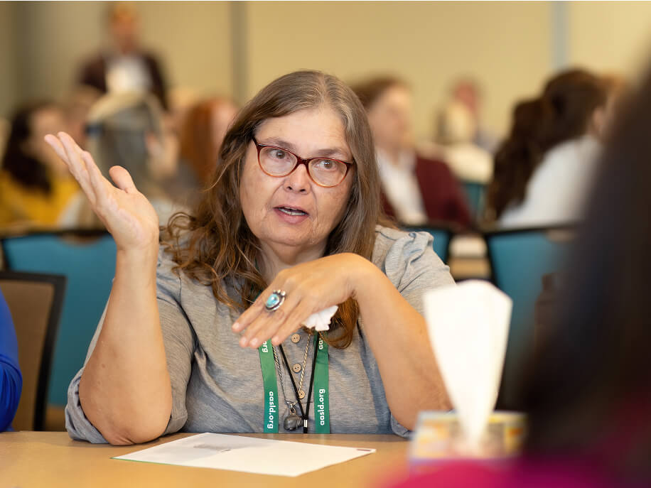 Kim, a MASH patient advocate, sits at a table talking to another woman 